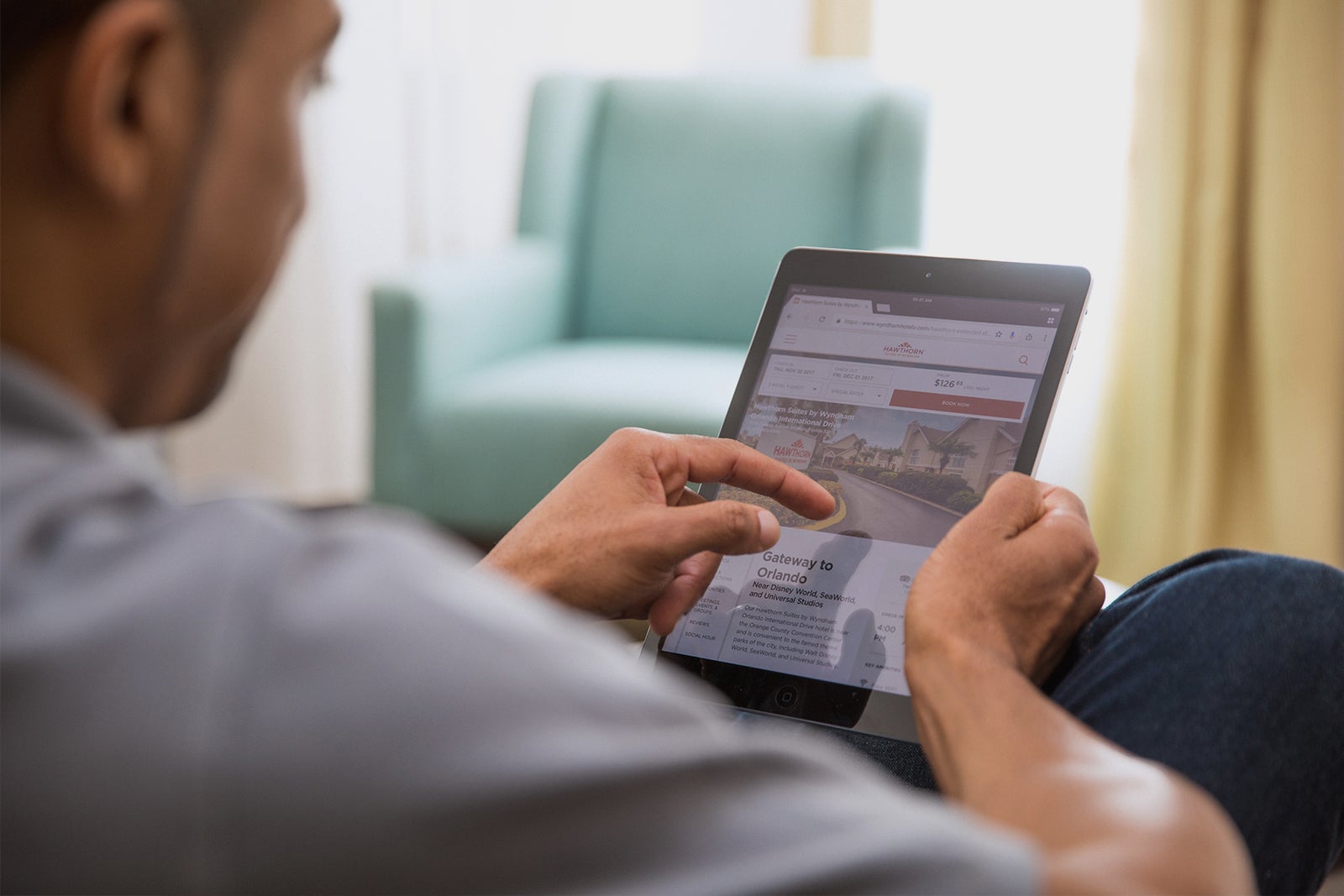 Person seated indoors with a tablet with a chair visible in the background 