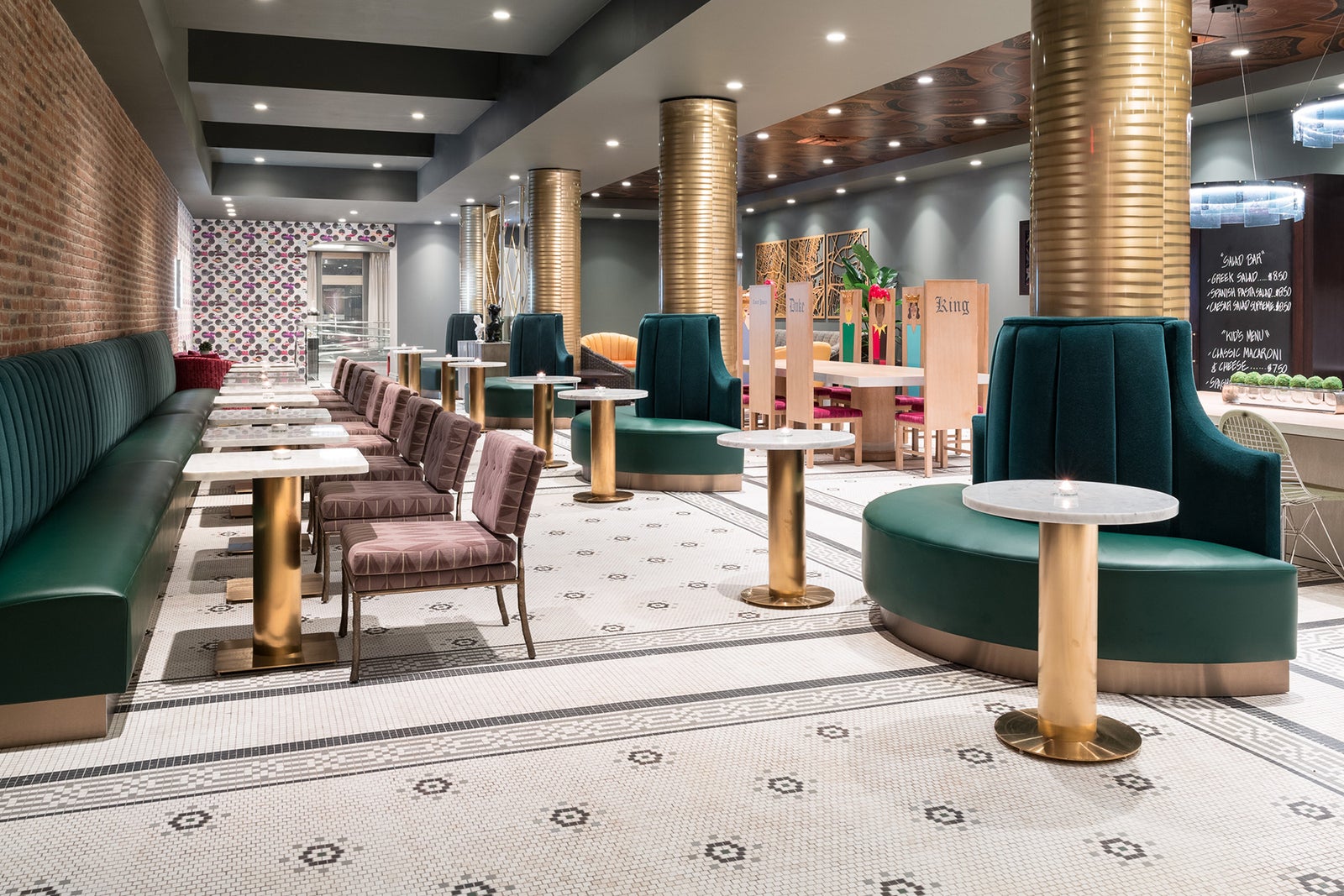 Interior of a restaurant lounge with green booths, patterned chairs, brass columns, marble tables, and a geometric mosaic-tile floor.