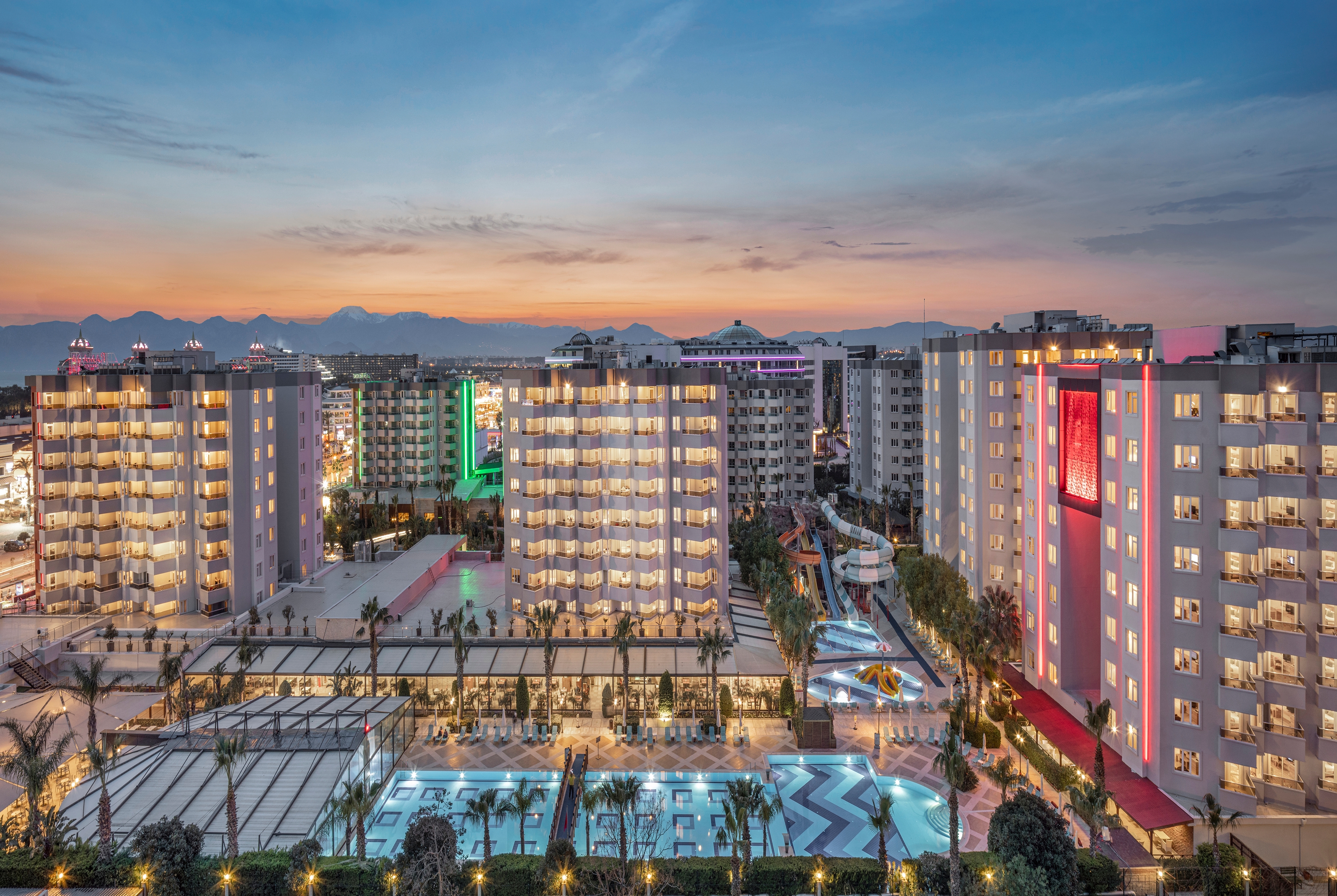Abendliche Außenansicht des Ramada Resort by Wyndham Lara mit Hotelgebäuden, Pool und Aquapark