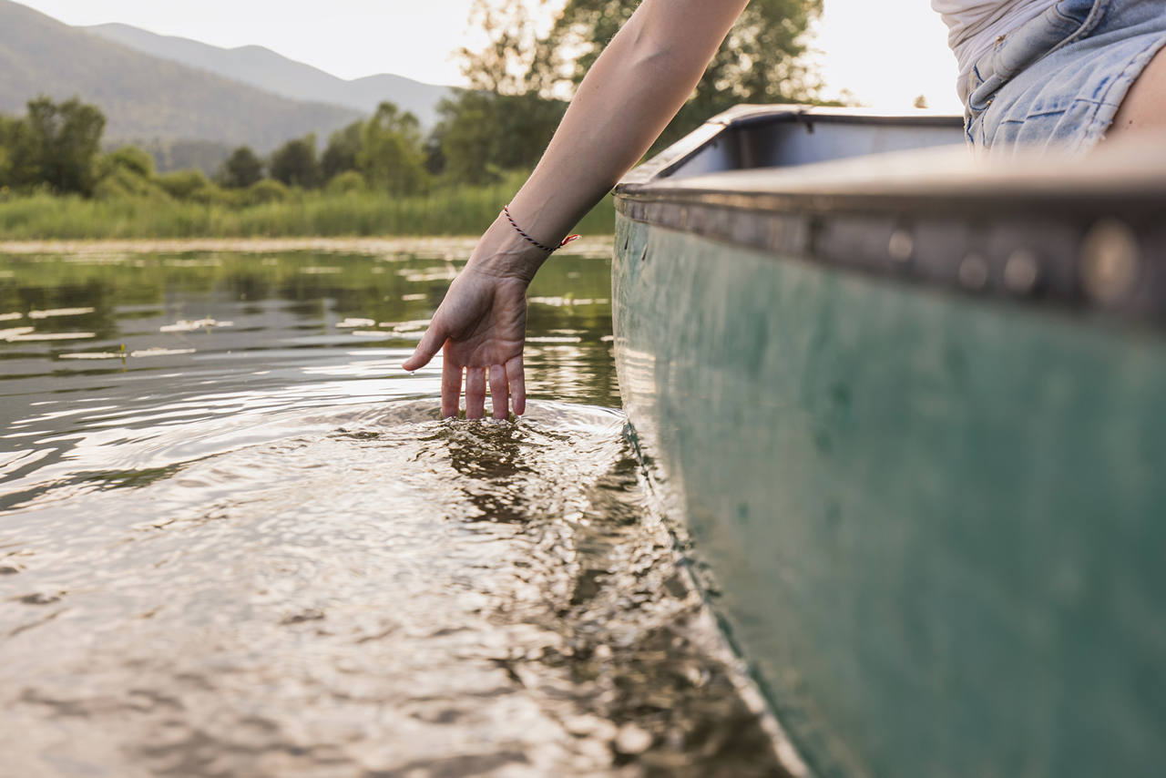 Person trailing a hand through the water beside a green canoe on a mountain lake.