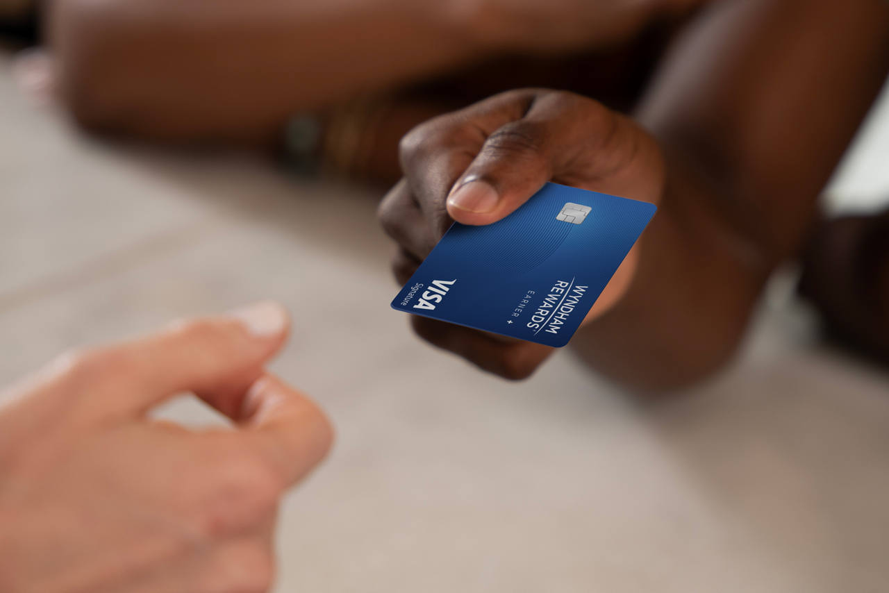 Wyndham Rewards Earner Plus card being handed across a table. 